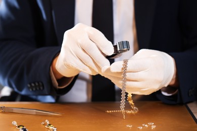 Photo of Appraiser with loupe evaluating luxury jewelry at table, closeup