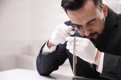 Photo of Appraiser evaluating luxury necklace at white table indoors, space for text