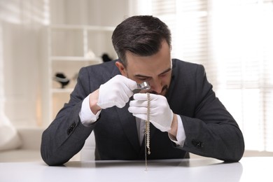 Photo of Appraiser evaluating luxury necklace at white table indoors