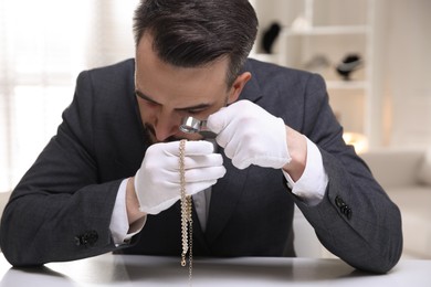 Photo of Appraiser evaluating luxury necklace at white table indoors