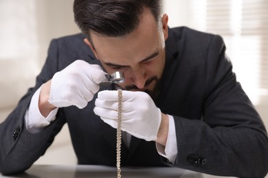 Photo of Appraiser evaluating luxury necklace at table indoors