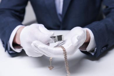 Photo of Appraiser evaluating luxury necklace at white table indoors, closeup