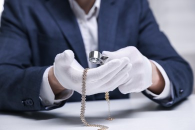 Photo of Appraiser evaluating luxury necklace at white table indoors, closeup