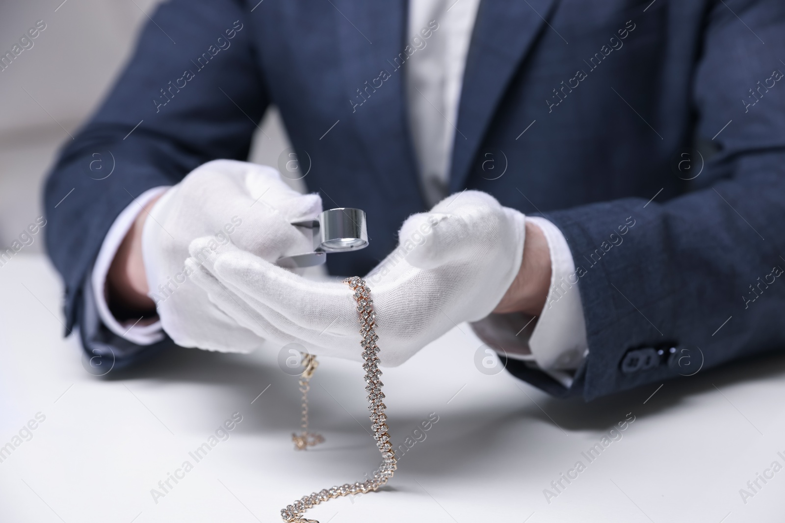 Appraiser evaluating luxury necklace at white table indoors, closeup Photo of Appraiser evaluating luxury necklace at white table indoors, closeup