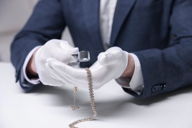 Photo of Appraiser evaluating luxury necklace at white table indoors, closeup