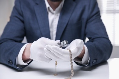 Photo of Appraiser evaluating luxury necklace at white table indoors, closeup