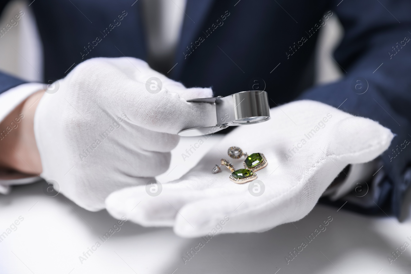 Appraiser evaluating luxury earrings at white table indoors, closeup Photo of Appraiser evaluating luxury earrings at white table indoors, closeup