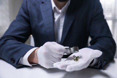 Photo of Appraiser evaluating luxury earrings at white table indoors, closeup