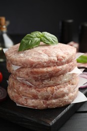 Photo of Fresh raw patties for burger and basil on black wooden table, closeup