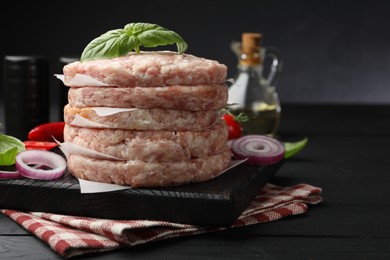 Photo of Fresh raw patties for burger and spices on black wooden table, closeup. Space for text