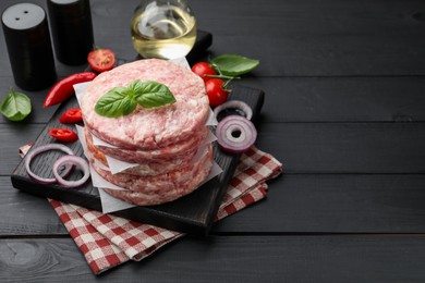 Photo of Fresh raw patties for burger, spices and tomatoes on black wooden table, closeup. Space for text