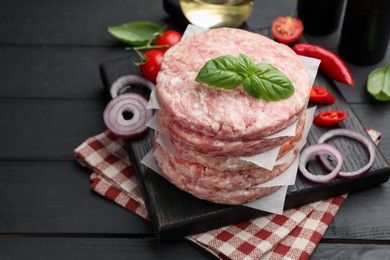 Photo of Fresh raw patties for burger, spices and tomatoes on black wooden table, closeup. Space for text