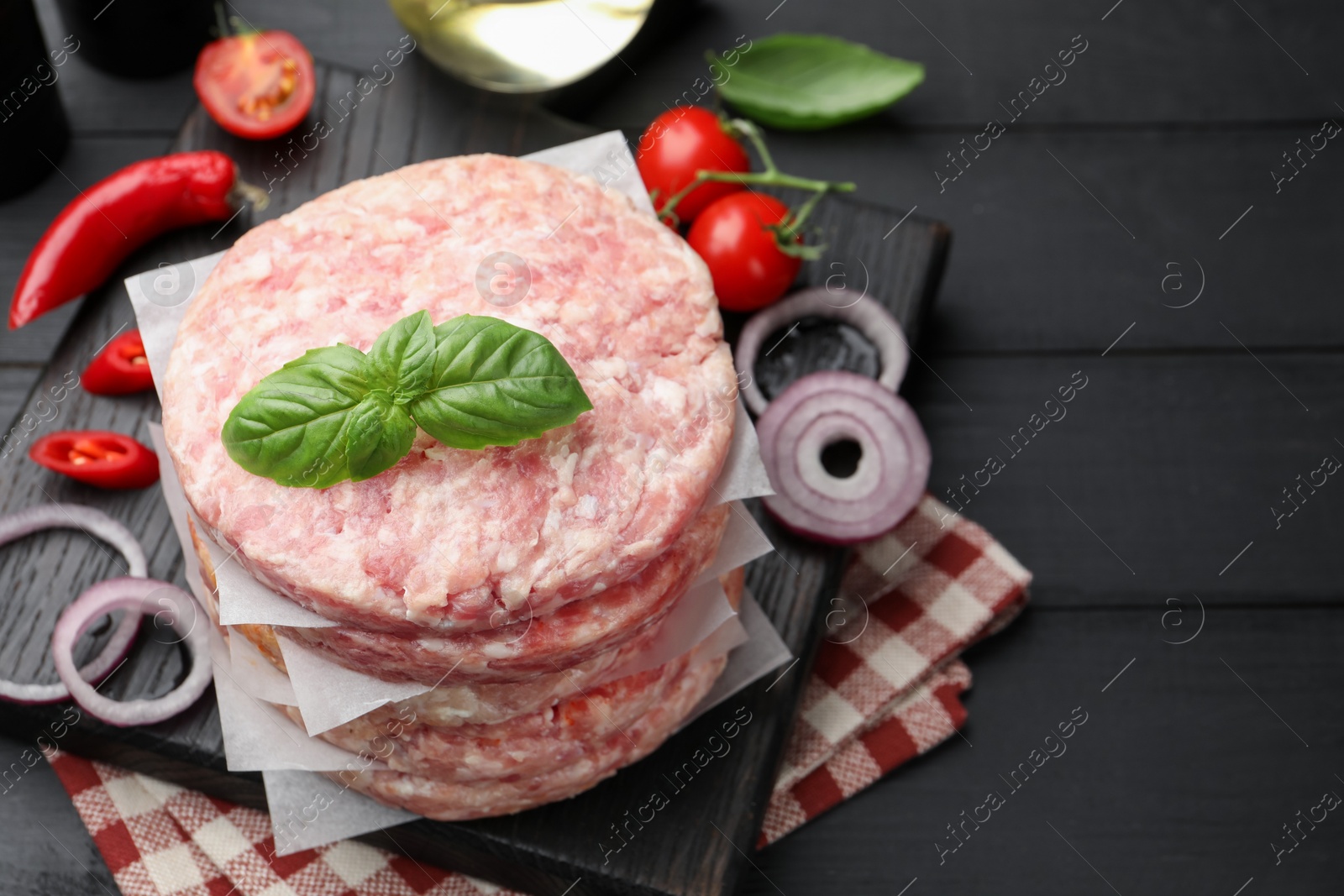 Fresh raw patties for burger, spices and tomatoes on black wooden table, above view. Space for text Photo of Fresh raw patties for burger, spices and tomatoes on black wooden table, above view. Space for text