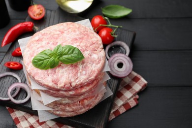 Photo of Fresh raw patties for burger, spices and tomatoes on black wooden table, above view. Space for text