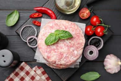 Photo of Fresh raw patties for burger, spices and tomatoes on black wooden table, flat lay