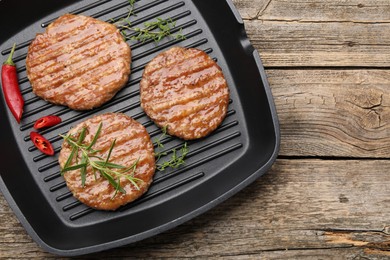 Photo of Delicious hamburger patties and spices in frying pan on wooden table, top view. Space for text