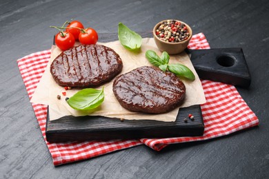 Photo of Delicious hamburger patties, tomatoes and spices on black table, closeup