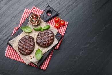 Photo of Delicious hamburger patties, tomatoes and spices on black table, flat lay. Space for text