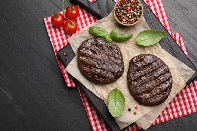Photo of Delicious hamburger patties, tomatoes and spices on black table, flat lay. Space for text