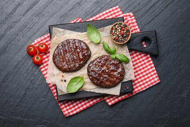 Photo of Delicious hamburger patties, tomatoes and spices on black table, flat lay