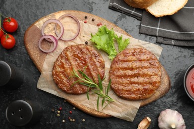Photo of Delicious hamburger patties, tomatoes and spices on black table, flat lay