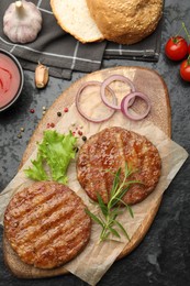 Photo of Delicious hamburger patties, tomatoes and spices on black table, flat lay