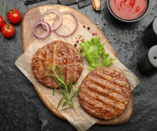 Photo of Delicious hamburger patties, tomatoes and spices on black table, flat lay