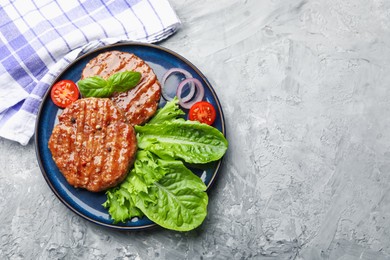 Photo of Delicious hamburger patties, tomato, lettuce and spices on grey table, top view. Space for text