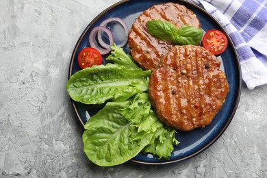 Photo of Delicious hamburger patties, tomato, lettuce and spices on grey table, top view