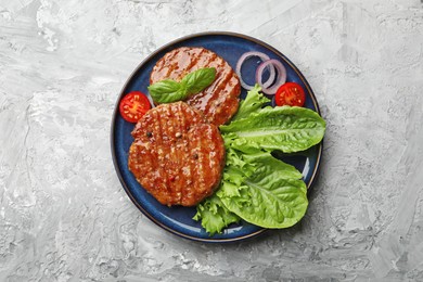 Photo of Delicious hamburger patties, tomato, lettuce and spices on grey table, top view