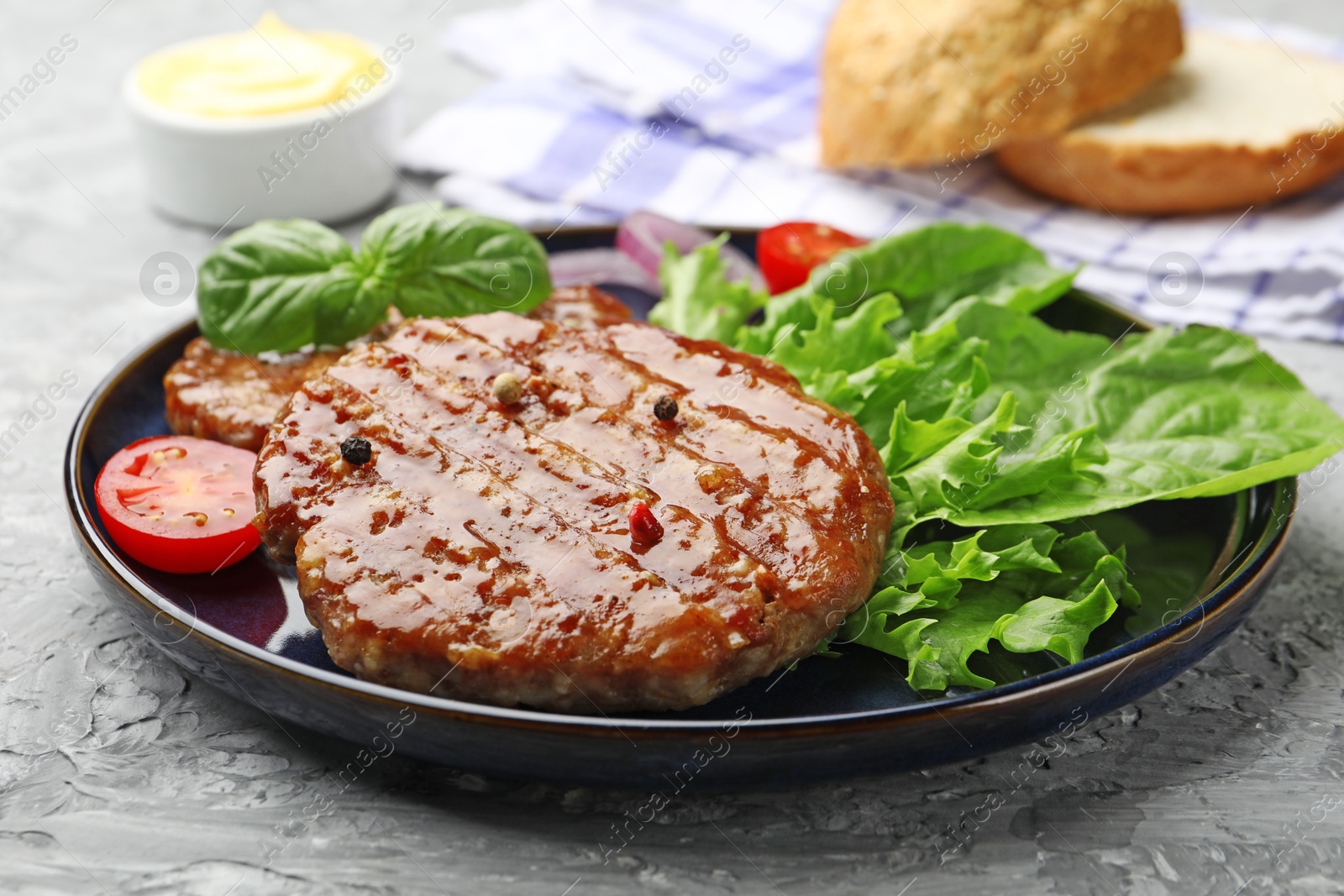 Delicious hamburger patties, tomato, lettuce, buns and spices on grey table, closeup Photo of Delicious hamburger patties, tomato, lettuce, buns and spices on grey table, closeup