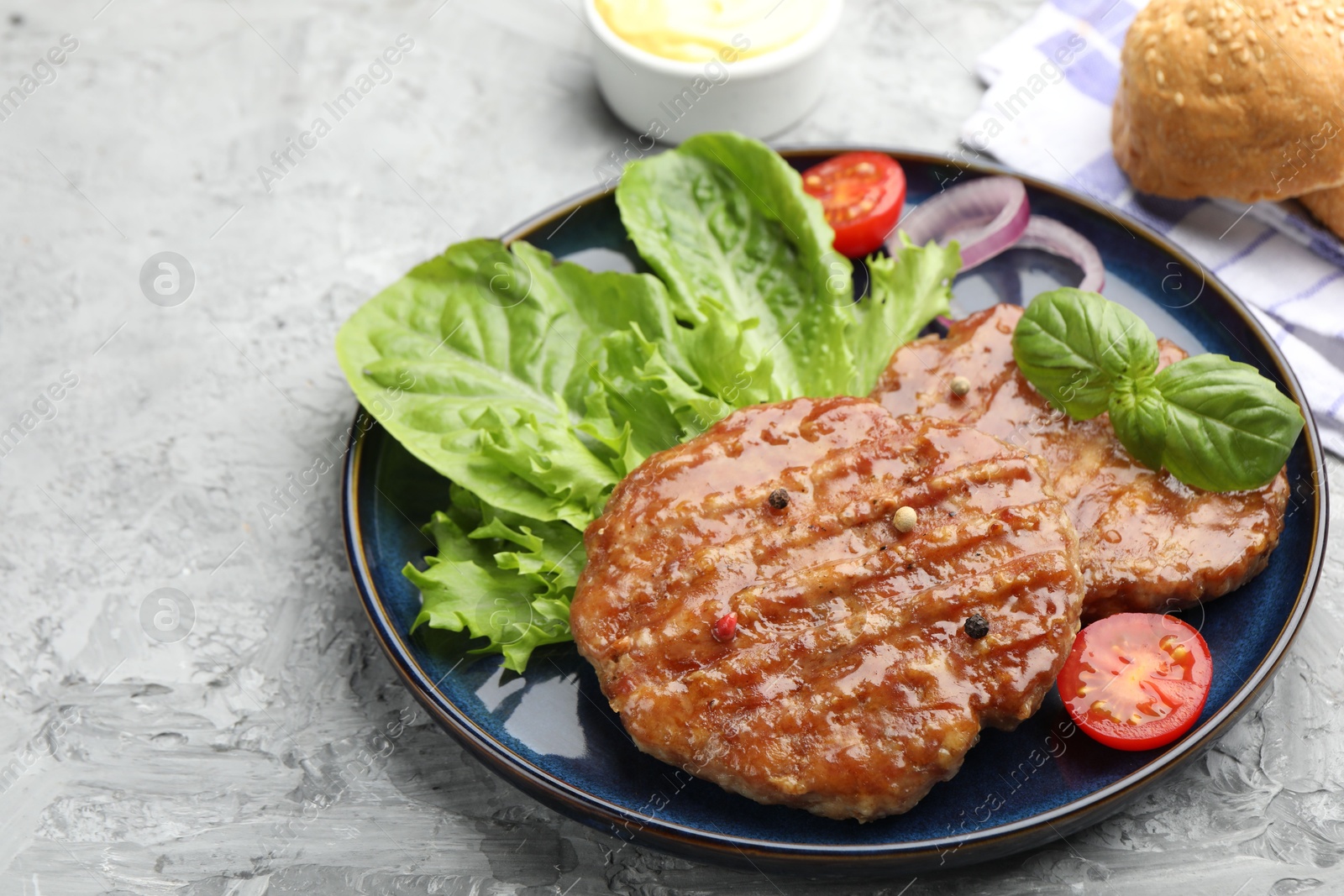 Delicious hamburger patties, tomato, lettuce, buns and spices on grey table, closeup. Space for text Photo of Delicious hamburger patties, tomato, lettuce, buns and spices on grey table, closeup. Space for text
