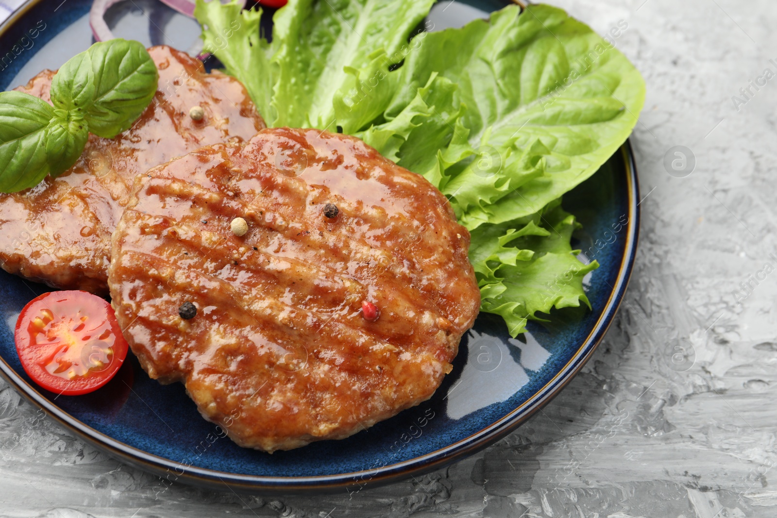 Delicious hamburger patties, tomato, lettuce and spices on grey table, closeup Photo of Delicious hamburger patties, tomato, lettuce and spices on grey table, closeup