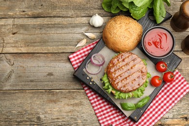 Photo of Delicious hamburger patty, bun, vegetables and spices on wooden table, flat lay. Space for text
