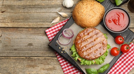 Photo of Delicious hamburger patty, bun, vegetables and spices on wooden table, flat lay. Space for text