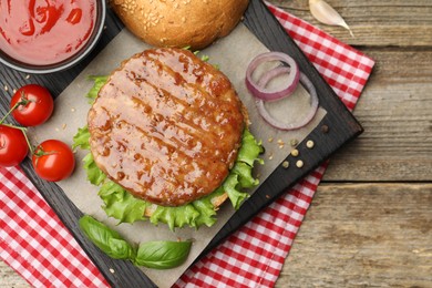 Photo of Delicious hamburger patty, bun, vegetables and spices on wooden table, flat lay