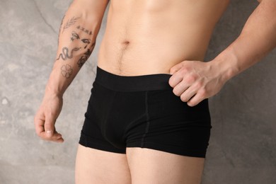 Photo of Young man in stylish black underwear near grey wall indoors, closeup