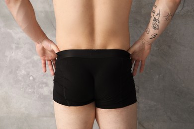 Photo of Young man in stylish black underwear near grey wall indoors, closeup