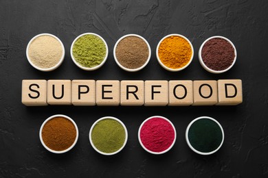 Photo of Different superfoods and word made of cubes on dark textured table, flat lay