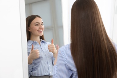 Photo of Beautiful woman showing thumbs up near mirror indoors