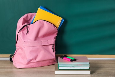 Photo of Backpack with workbooks, notebooks, book and highlighters on wooden table near blackboard, space for text