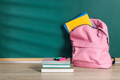 Photo of Backpack with workbooks, notebooks, book and highlighters on wooden table near blackboard, space for text