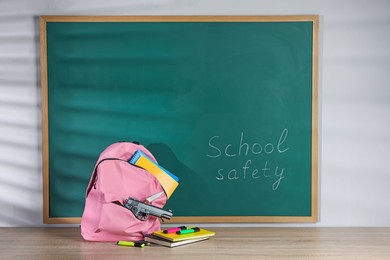 Photo of Backpack with gun, knife and stationery on wooden table near blackboard. School safety