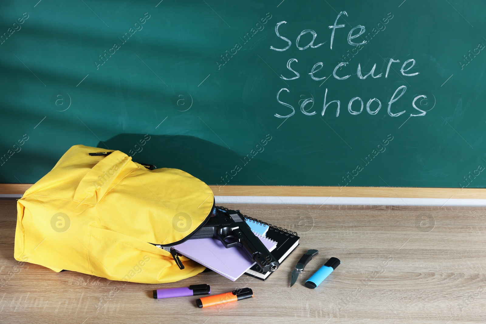 Backpack, gun, knife and stationery on wooden table near blackboard with words Safe Secure Schools Photo of Backpack, gun, knife and stationery on wooden table near blackboard with words Safe Secure Schools
