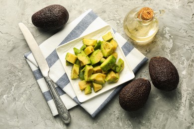 Photo of Tasty cut avocados with dressing and knife on grey textured table, flat lay