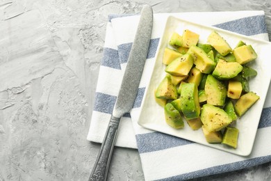 Photo of Tasty cut avocados with dressing and knife on grey textured table, top view. Space for text
