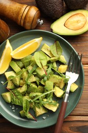 Photo of Tasty cut avocados with arugula, lemon and dressing on wooden table, flat lay