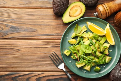 Photo of Tasty cut avocados with arugula, lemon and dressing on wooden table, flat lay. Space for text
