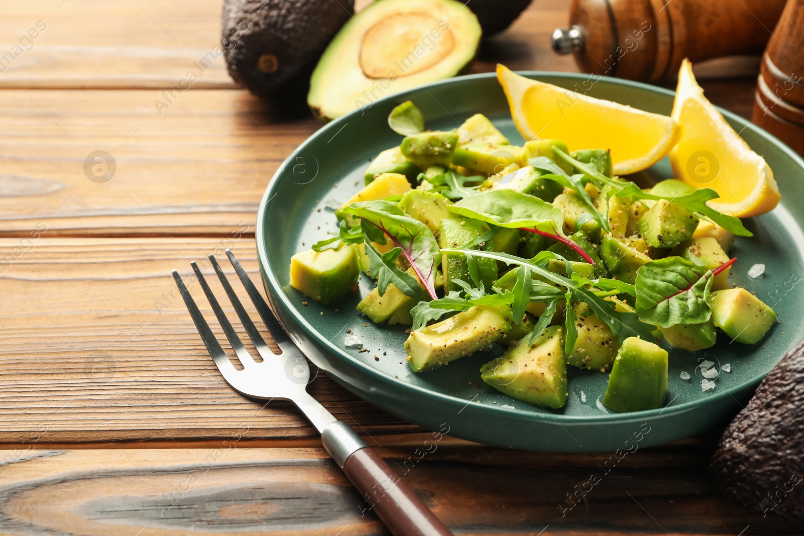 Tasty cut avocados with arugula, lemon and dressing on wooden table, closeup Photo of Tasty cut avocados with arugula, lemon and dressing on wooden table, closeup