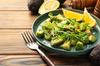 Photo of Tasty cut avocados with arugula, lemon and dressing on wooden table, closeup